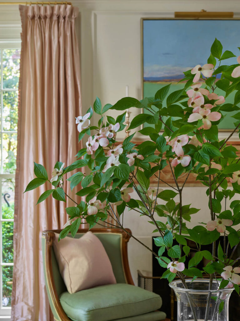 Pink blossoms in a vase next to a chair with luxurious curtains behind Atlanta